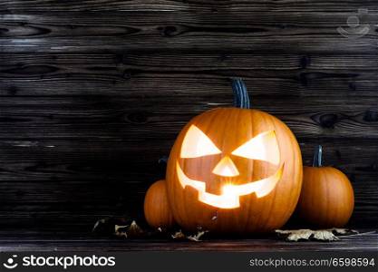 Halloween pumpkins head jack o lantern and dry maple leaves on wooden background. Halloween pumpkins and dry leaves