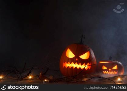 Halloween pumpkins head jack o lantern, candles and dry maple leaves in mist. Halloween pumpkins in mist