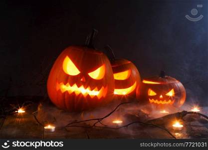 Halloween pumpkins head jack o lantern, candles and dry maple leaves in mist. Halloween pumpkins head jack o lantern