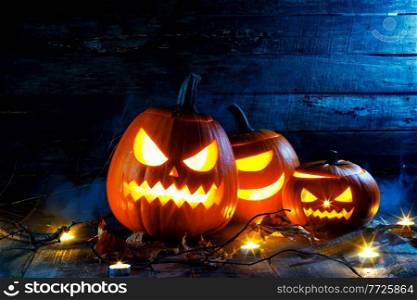 Halloween pumpkins head jack o lantern, candles and dry maple leaves in mist. Halloween pumpkins head jack o lantern