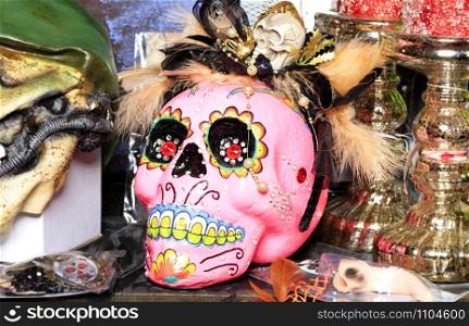 Halloween, skull dolls with a smile, decorated with female cosmetics in a hat with feathers, isolated on a blurred background of Halloween accessories.. Halloween, pink skull doll with female makeup and a hat with feathers isolated on a blurred background.