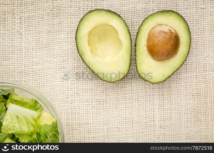 halved avocado and a bowl of romaine lettuce against burlap canvas