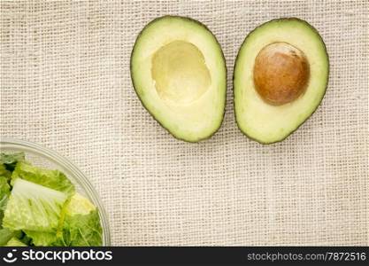 halved avocado and a bowl of romaine lettuce against burlap canvas