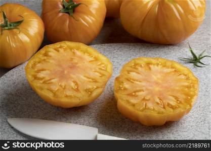 Halved juicy yellow coeur de boeuf tomato close up and whole ones in the background