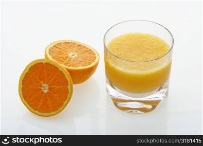 Halved orange and glass of orange juice on white background.