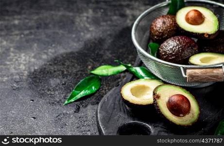 Halves and a whole avocado in a colander. On a black background. High quality photo. Halves and a whole avocado in a colander.
