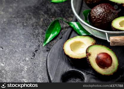 Halves and a whole avocado in a colander. On a black background. High quality photo. Halves and a whole avocado in a colander.