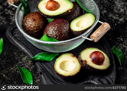 Halves and a whole avocado in a colander. On a black background. High quality photo. Halves and a whole avocado in a colander.