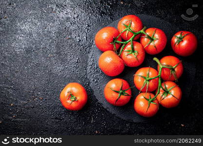 Halves and whole tomatoes on a branch on a stone board. On a black background. High quality photo. Halves and whole tomatoes on a branch on a stone board.