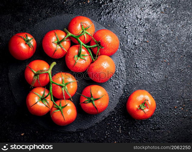 Halves and whole tomatoes on a branch on a stone board. On a black background. High quality photo. Halves and whole tomatoes on a branch on a stone board.