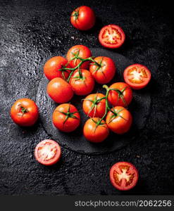 Halves and whole tomatoes on a branch on a stone board. On a black background. High quality photo. Halves and whole tomatoes on a branch on a stone board.