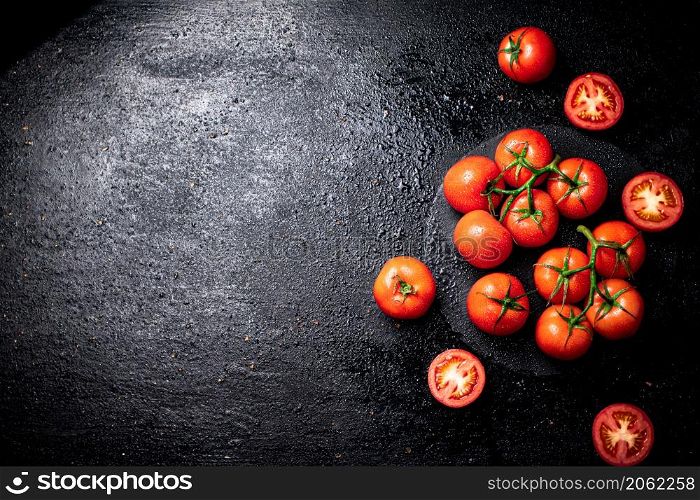 Halves and whole tomatoes on a branch on a stone board. On a black background. High quality photo. Halves and whole tomatoes on a branch on a stone board.