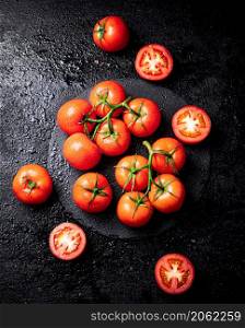 Halves and whole tomatoes on a branch on a stone board. On a black background. High quality photo. Halves and whole tomatoes on a branch on a stone board.