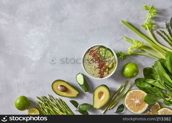 Halves of avocado, lime, cucumber, asparagus, spinach and a plate with freshly prepared smoothies with flax seeds on a gray concrete background with a copy of the space. Frame food. Top view. Fresh organic vegetables and a plate of smoothies with flax seeds on a gray concrete background with copy space. Top view