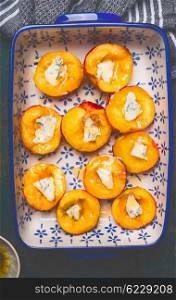 Halves of peaches in baking dish with cheese and honey, top view, close up. Summer fruits cooking