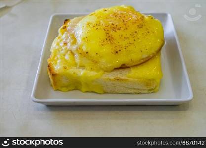 Ham and Cheese Stuffed French Toast on White table and sunny side up egg on top in square white plate