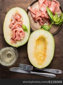 Ham and melon, antipasti with white wine in glass and cutlery on rustic wooden background, top view