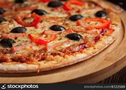 Ham pizza with capsicum and olives on wooden board on table close up. Ham pizza
