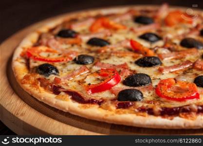 Ham pizza with capsicum and olives on wooden board on table close up. Ham pizza