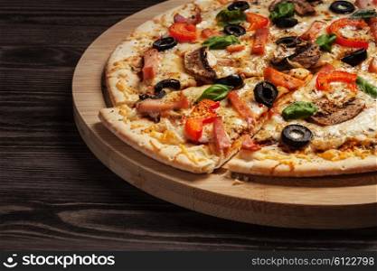 Ham pizza with capsicum, mushrooms, olives and basil leaves on wooden board on old table close up
