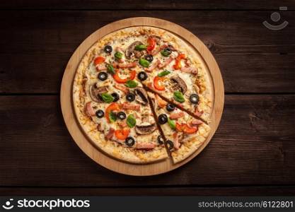 Ham pizza with capsicum, mushrooms, olives and basil leaves on wooden board on old table