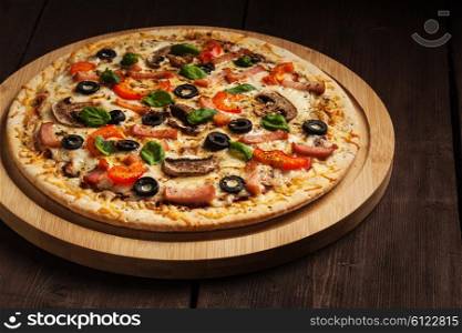 Ham pizza with capsicum, mushrooms, olives and basil leaves on wooden board on old table