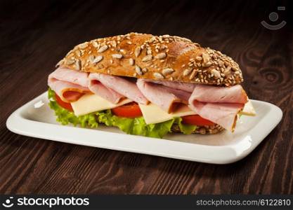 Ham sandwich with lettuce, cheese, tomato on plate on wooden table