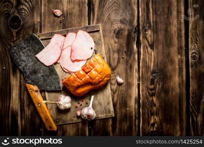 Ham with a hatchet and garlic on the Board. On wooden background.. Ham with a hatchet and garlic on the Board.