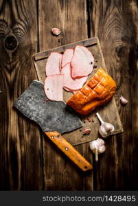 Ham with a hatchet and garlic on the Board. On wooden background.. Ham with a hatchet and garlic on the Board.