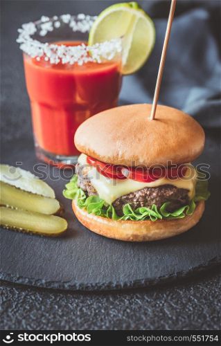 Hamburger with a glass of tomato juice on the black stone board