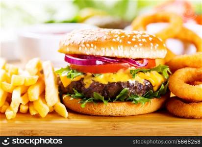 hamburger with fries and onion rings on wooden table
