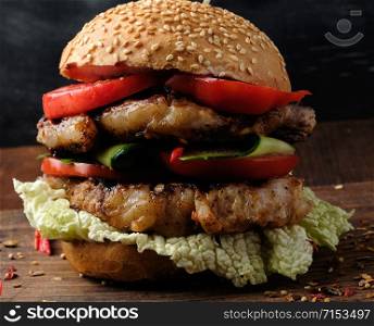 hamburger with pork fried steak, red tomatoes, fresh round bun with sesame seeds on a vintage brown wooden board
