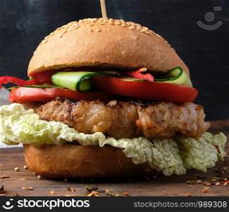 hamburger with pork fried steak, red tomatoes, fresh round bun with sesame seeds on a vintage brown wooden board