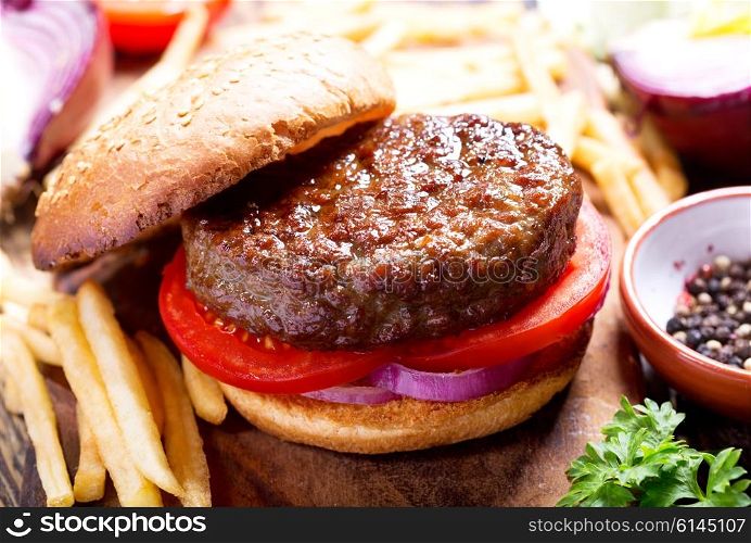hamburger with vegetables and fries on a wooden board