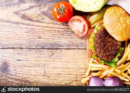 hamburger with vegetables and fries on a wooden board, top view.