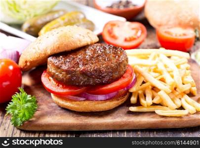 hamburger with vegetables and fries on a wooden table
