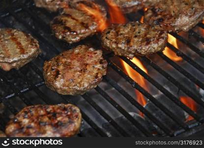 Hamburgers cooking on barbeque grill with flames