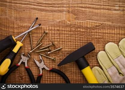 hamer pliers screwdriwer and gloves on woodn board