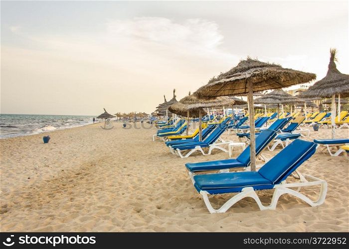Hammamet beach with shades made of straw, blue beach chairs and beautiful white sand along the coast of the Mediterranean sea
