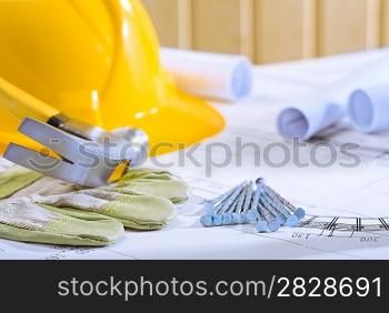 hammer on glowe and nails with helmet on blueprints