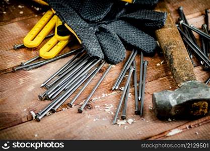 Hammer with nails and gloves on the table. On a wooden background. High quality photo. Hammer with nails and gloves on the table.