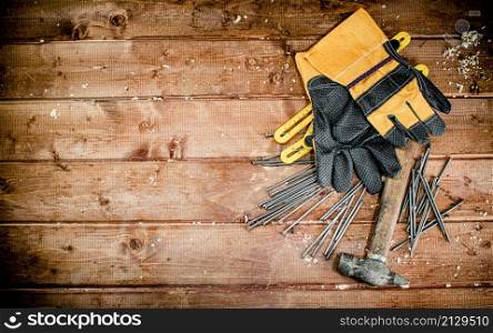 Hammer with nails and gloves on the table. On a wooden background. High quality photo. Hammer with nails and gloves on the table.