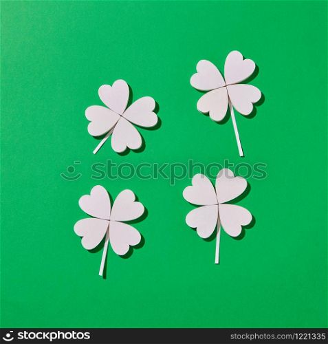 Hancraft shamrock plant composition from white petals in the shape of hearts on a green background with hard shadows, copy space. Happy St.Patrick &rsquo;s Day concept.. Four handmade shamrock&rsquo;s leaves with shadows.