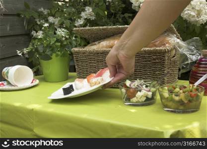 Hand adding a plate of sushi to the picknick table outdoors
