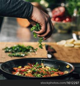 Hand Adding Parsley into a frying pan with vegetables. Vegan restaurant cooking.. Hand Adding Parsley into Frying Pan with Vegetables