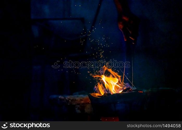 Hand adjust burning charcoal for cooking with flame and fire spark on dark background