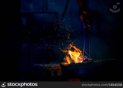 Hand adjust burning charcoal for cooking with flame and fire spark on dark background