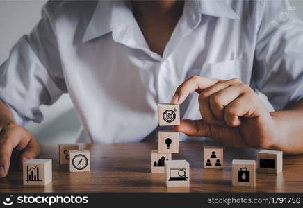 Hand adult Asian man holding of dart board icon on cube block. Business management, finance, strategy, marketing. wood block with icons concept. Human resource management, Strategy target planning.