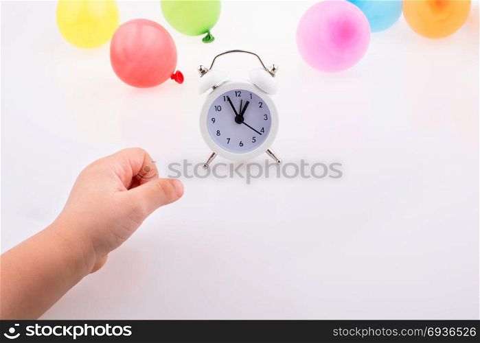 Hand and alarm clock with balloons on the white background