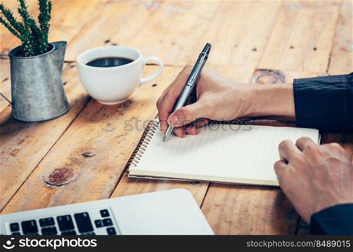 Hand business man writing notebook on wood table in coffee shop.